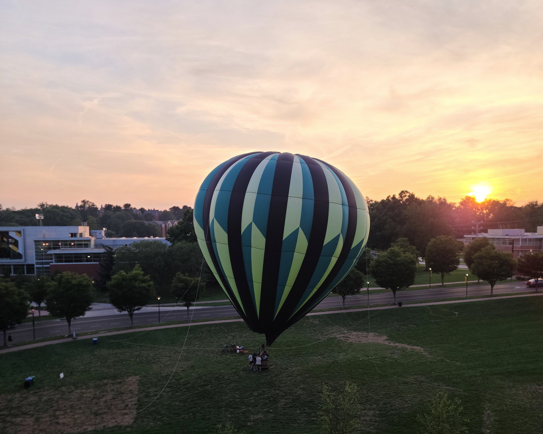 A hot-air balloon glows above a dark tree line at sunset.